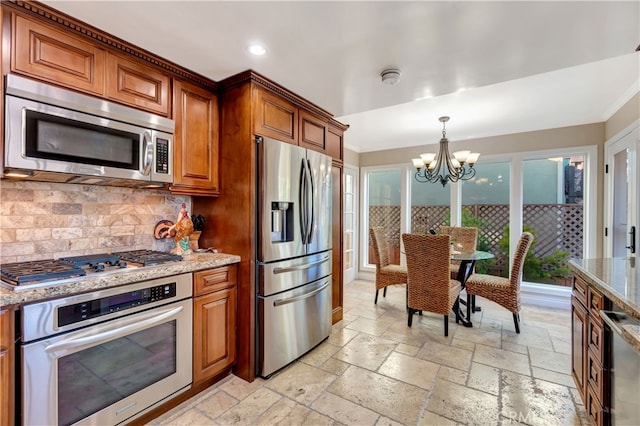 kitchen featuring appliances with stainless steel finishes, hanging light fixtures, backsplash, light stone countertops, and an inviting chandelier