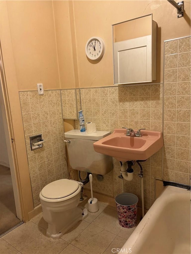 bathroom with a tub to relax in, sink, tile walls, tile patterned flooring, and toilet