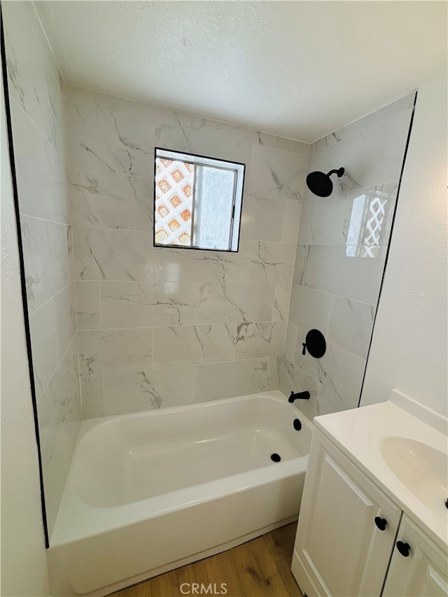 bathroom with wood-type flooring, a textured ceiling, tiled shower / bath, and vanity