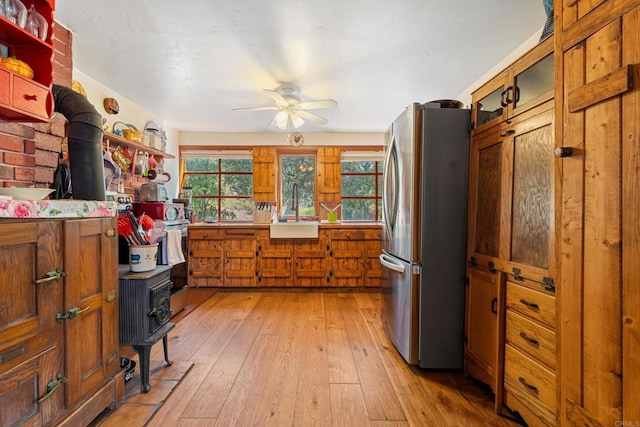 kitchen featuring light wood-type flooring, sink, a wood stove, and stainless steel refrigerator