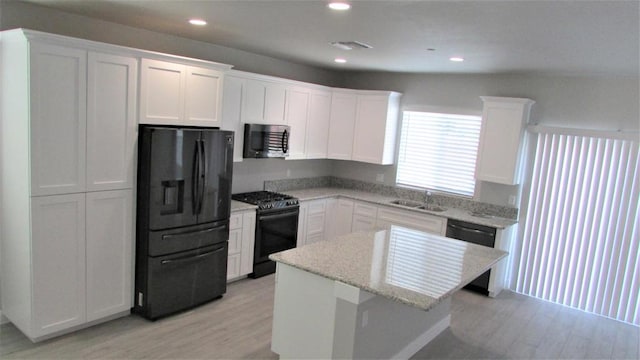 kitchen featuring light stone counters, a kitchen island, white cabinetry, and black appliances