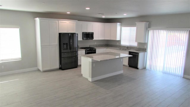 kitchen featuring a wealth of natural light, black appliances, white cabinetry, and a kitchen island