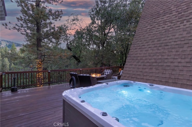 pool at dusk featuring a wooden deck, a hot tub, and an outdoor fire pit