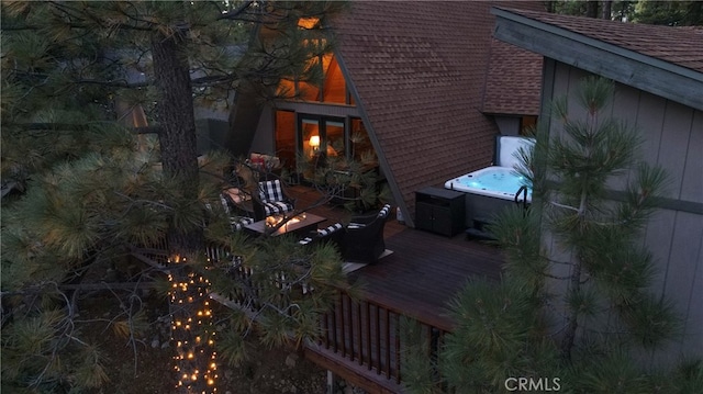 view of side of property with roof with shingles, a hot tub, and a wooden deck