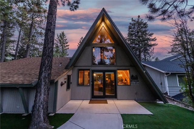 back house at dusk featuring a yard and a patio