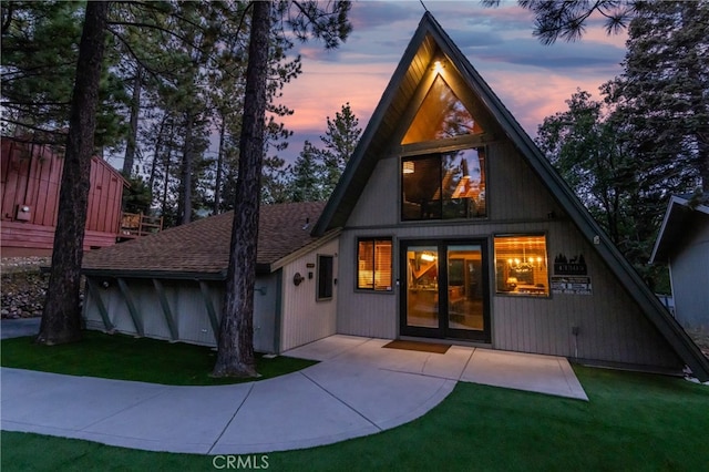 back of property at dusk with a patio, roof with shingles, and a lawn