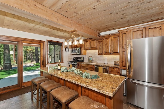 kitchen with brown cabinetry, light stone counters, appliances with stainless steel finishes, backsplash, and a sink