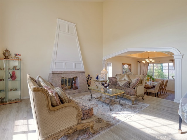 living room with a premium fireplace, light hardwood / wood-style floors, an inviting chandelier, and ornate columns