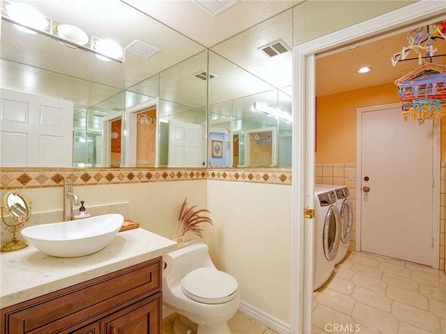 bathroom featuring tile walls, washing machine and dryer, vanity, tile patterned flooring, and toilet