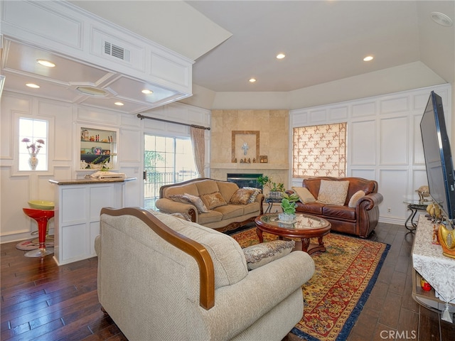 living room with a tile fireplace and dark wood-type flooring