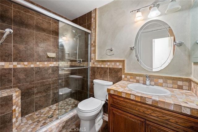 bathroom featuring vanity, toilet, tile walls, and a shower with shower door