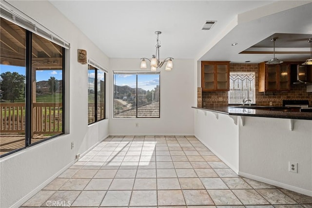 kitchen with hanging light fixtures, tasteful backsplash, a raised ceiling, a chandelier, and light tile patterned floors