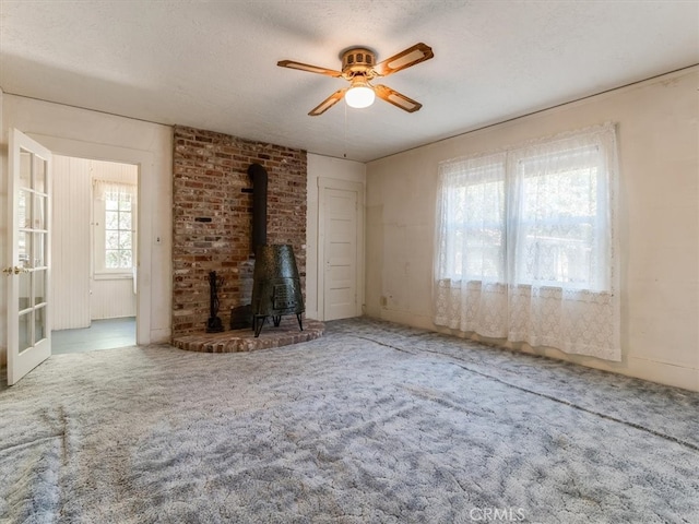 unfurnished living room with a wood stove, ceiling fan, carpet flooring, and a textured ceiling