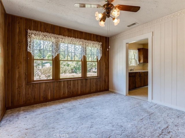 unfurnished room with light carpet, a wealth of natural light, ceiling fan, and wooden walls