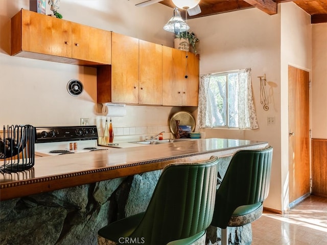 kitchen with kitchen peninsula, beamed ceiling, black range with electric cooktop, decorative light fixtures, and sink