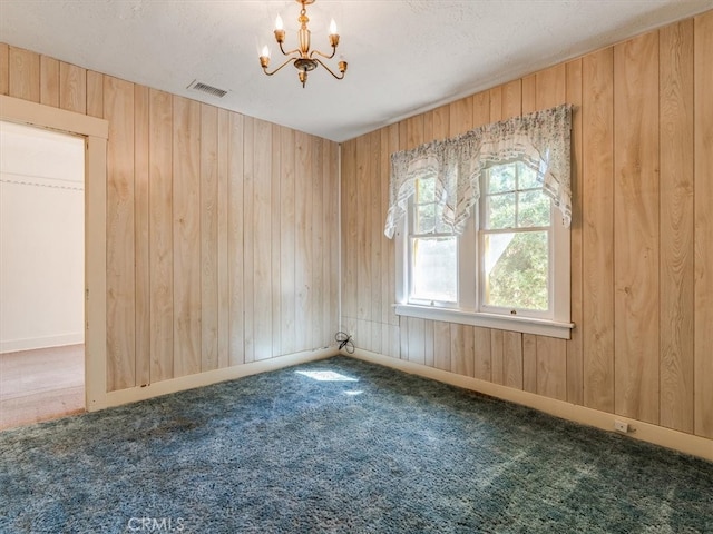 carpeted spare room featuring wooden walls and an inviting chandelier