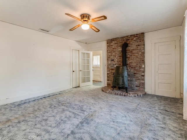 unfurnished living room with a wood stove, ceiling fan, and carpet floors