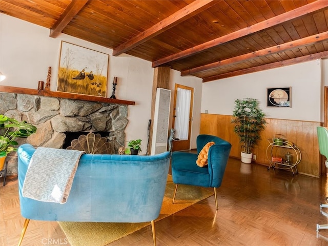 living room featuring wooden walls, beam ceiling, wooden ceiling, and a stone fireplace