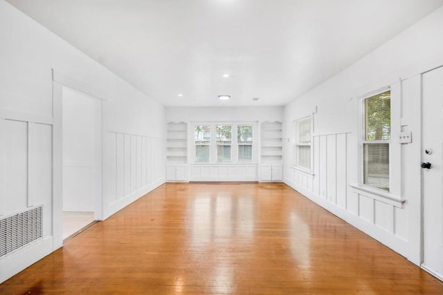 unfurnished living room featuring a wealth of natural light, built in features, and light hardwood / wood-style flooring