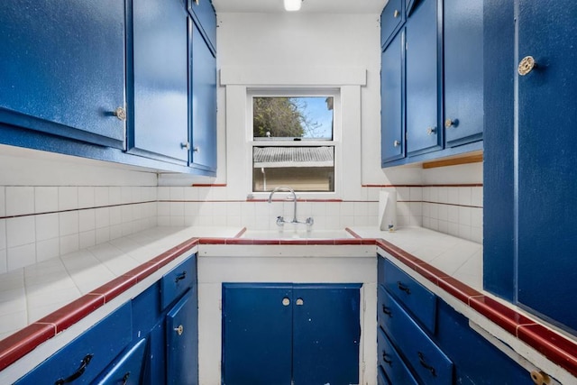 kitchen with decorative backsplash, blue cabinetry, sink, and tile counters