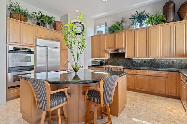 kitchen featuring decorative backsplash, appliances with stainless steel finishes, dark stone counters, sink, and an island with sink