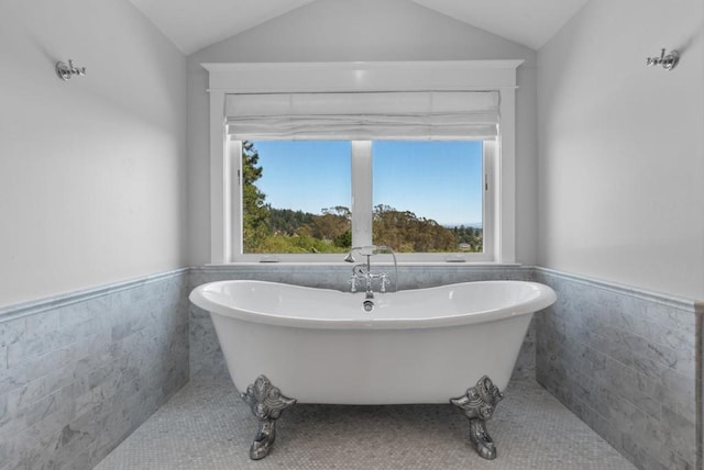 bathroom with a bathing tub, tile patterned flooring, tile walls, and vaulted ceiling