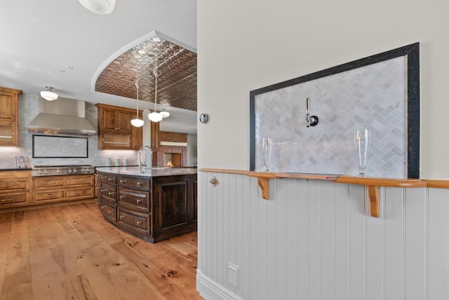 kitchen featuring decorative backsplash, wall chimney range hood, pendant lighting, light hardwood / wood-style flooring, and stainless steel gas stovetop