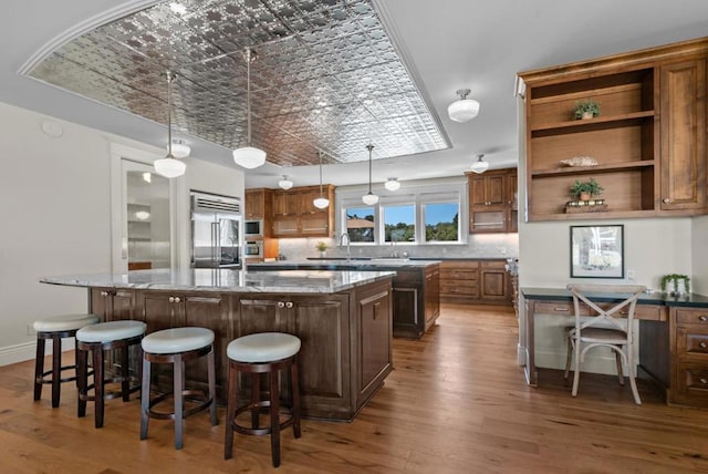 kitchen with a breakfast bar, a center island, built in appliances, light stone counters, and dark hardwood / wood-style flooring