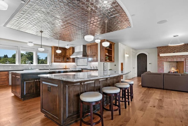 kitchen with wall chimney exhaust hood, light stone counters, pendant lighting, a breakfast bar area, and a fireplace