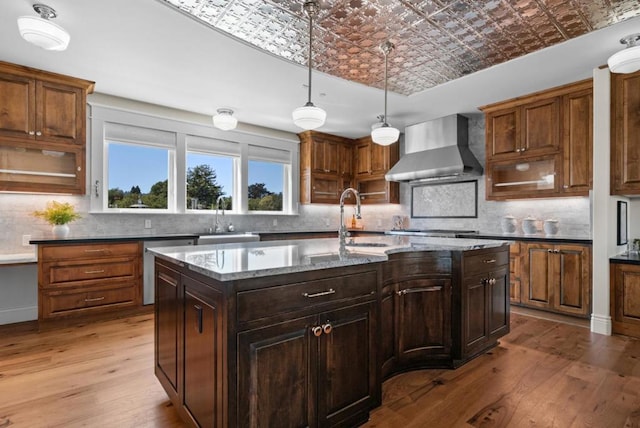 kitchen featuring sink, an island with sink, wall chimney range hood, and light hardwood / wood-style flooring