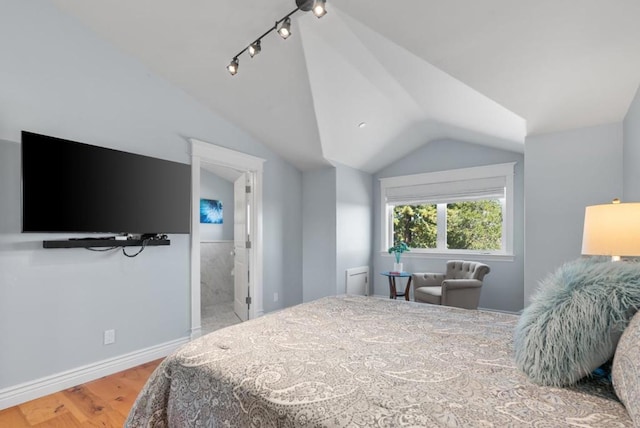 bedroom with hardwood / wood-style floors, ensuite bathroom, and vaulted ceiling