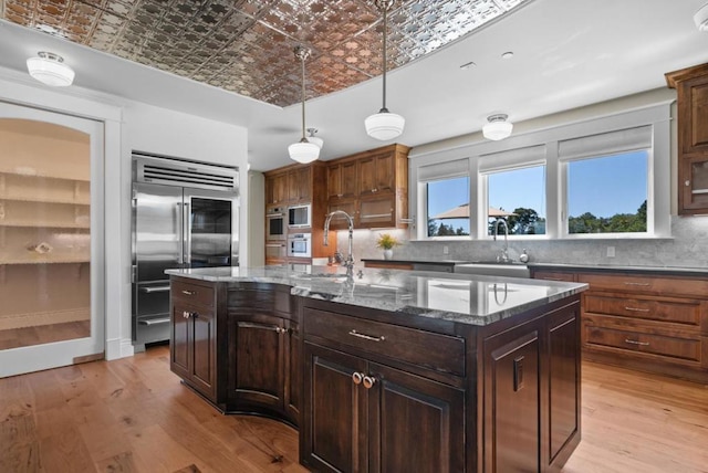 kitchen with built in appliances, sink, a kitchen island, and light hardwood / wood-style flooring