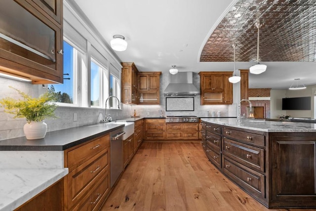 kitchen with appliances with stainless steel finishes, light wood-type flooring, wall chimney range hood, decorative light fixtures, and dark stone countertops