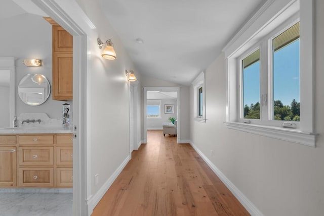 hallway featuring light hardwood / wood-style floors, lofted ceiling, and sink