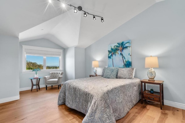 bedroom with hardwood / wood-style flooring, track lighting, and lofted ceiling