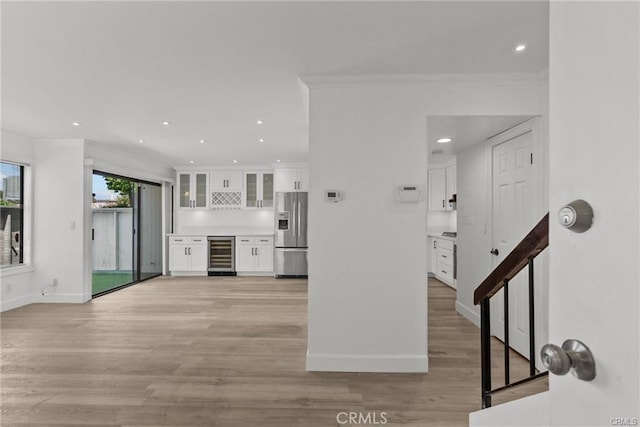 kitchen with stainless steel refrigerator with ice dispenser, light wood-type flooring, ornamental molding, white cabinets, and wine cooler