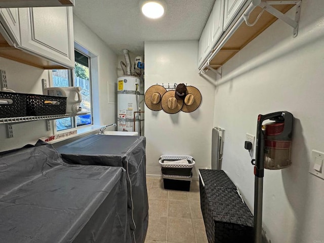 clothes washing area featuring independent washer and dryer, a textured ceiling, secured water heater, cabinets, and light tile patterned floors