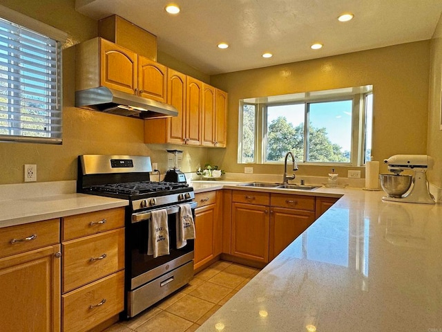 kitchen with light stone countertops, stainless steel range with gas cooktop, sink, and light tile patterned floors