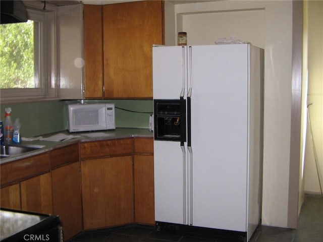 kitchen with dark tile patterned floors, white appliances, and sink