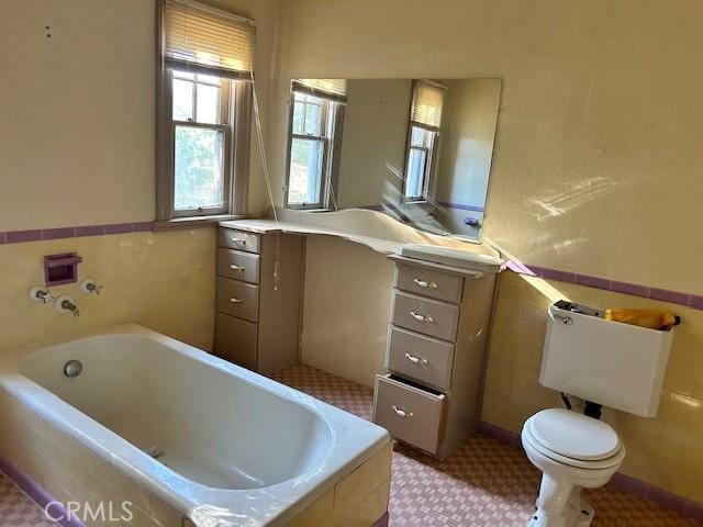 bathroom with toilet, tile walls, and tiled tub