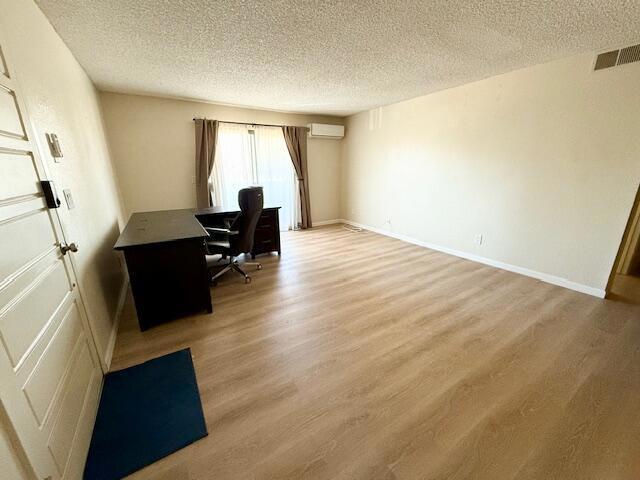 office featuring a textured ceiling, light hardwood / wood-style flooring, and a wall mounted air conditioner