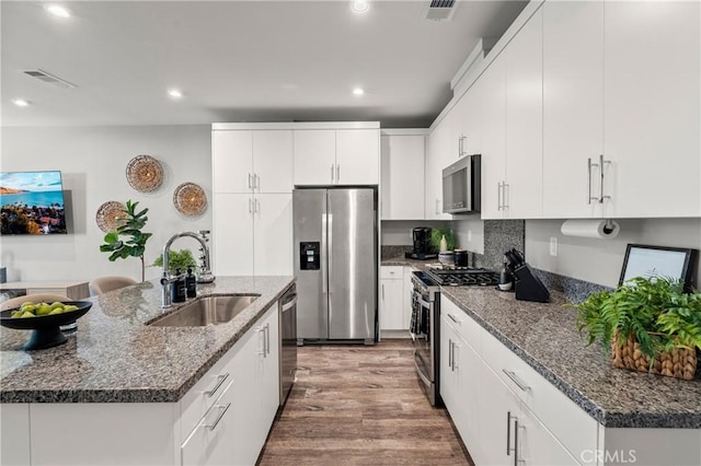 kitchen with white cabinets, a center island with sink, sink, appliances with stainless steel finishes, and light hardwood / wood-style floors