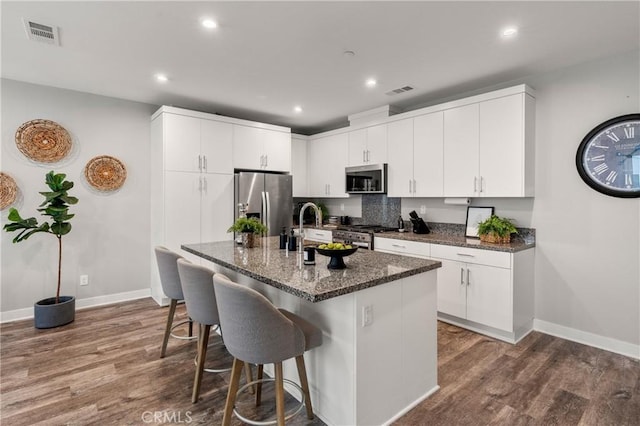 kitchen featuring white cabinets, hardwood / wood-style floors, stainless steel appliances, and dark stone countertops