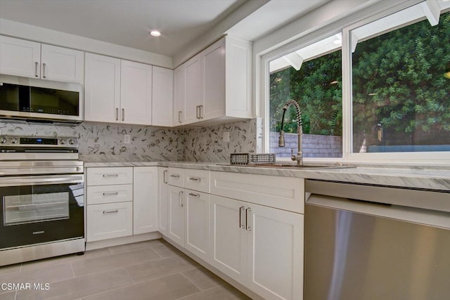 kitchen with light tile patterned floors, stainless steel appliances, white cabinets, light stone counters, and sink