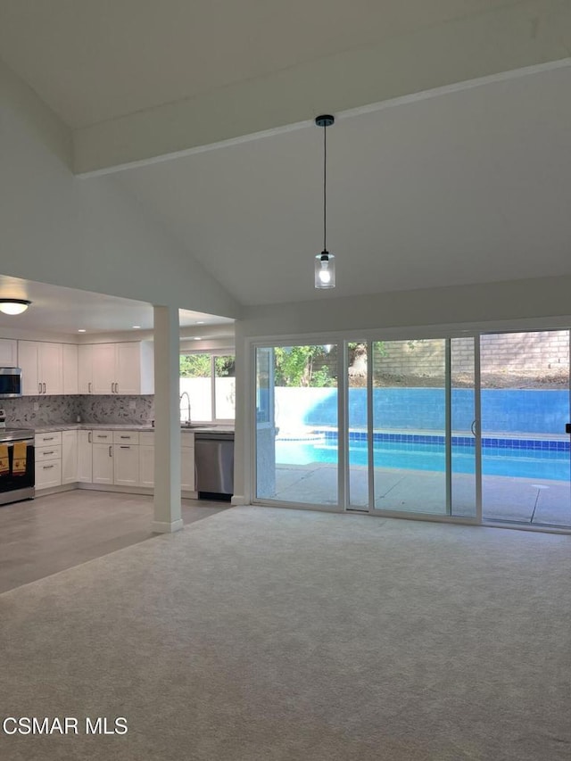 unfurnished living room with beam ceiling, light carpet, sink, and high vaulted ceiling