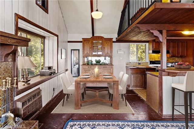 kitchen with pendant lighting, a high ceiling, wooden walls, tasteful backsplash, and beamed ceiling