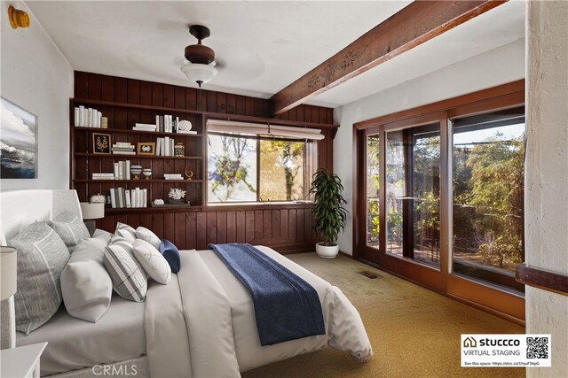 carpeted bedroom with beam ceiling, access to outside, ceiling fan, and wooden walls