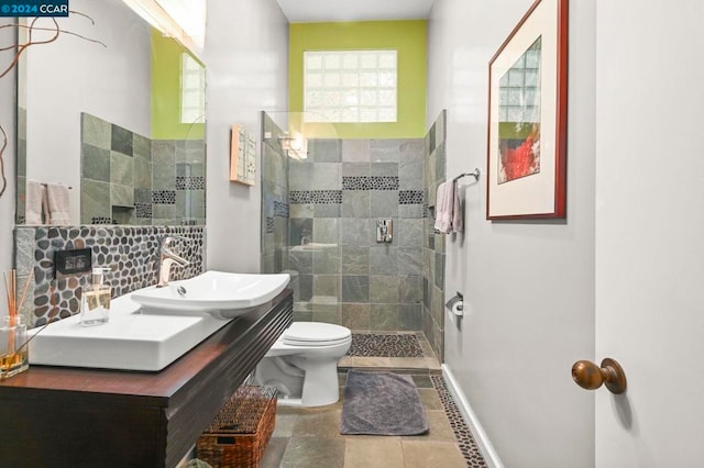 bathroom with toilet, tile patterned flooring, sink, and tiled shower