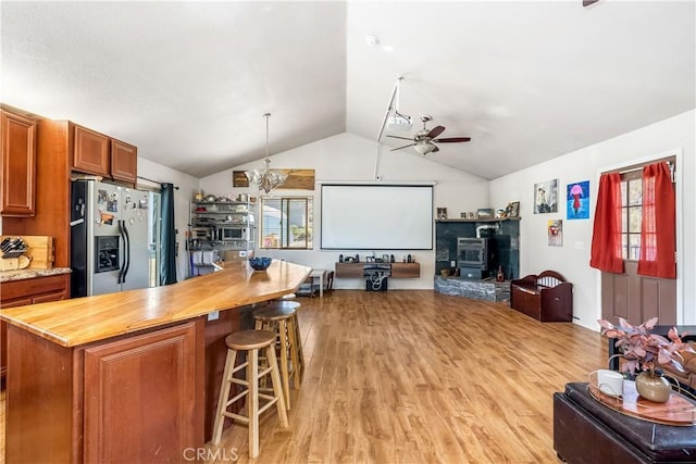 kitchen featuring wood counters, a wood stove, stainless steel refrigerator with ice dispenser, hanging light fixtures, and light hardwood / wood-style floors