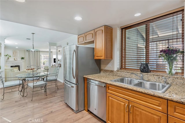 kitchen featuring light wood-type flooring, light stone counters, sink, appliances with stainless steel finishes, and decorative light fixtures